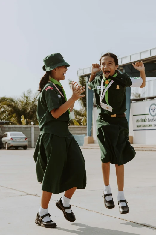 a couple of girls that are jumping in the air, a cartoon, trending on unsplash, wearing headmistress uniform, thailand, boy scout troop, deep green