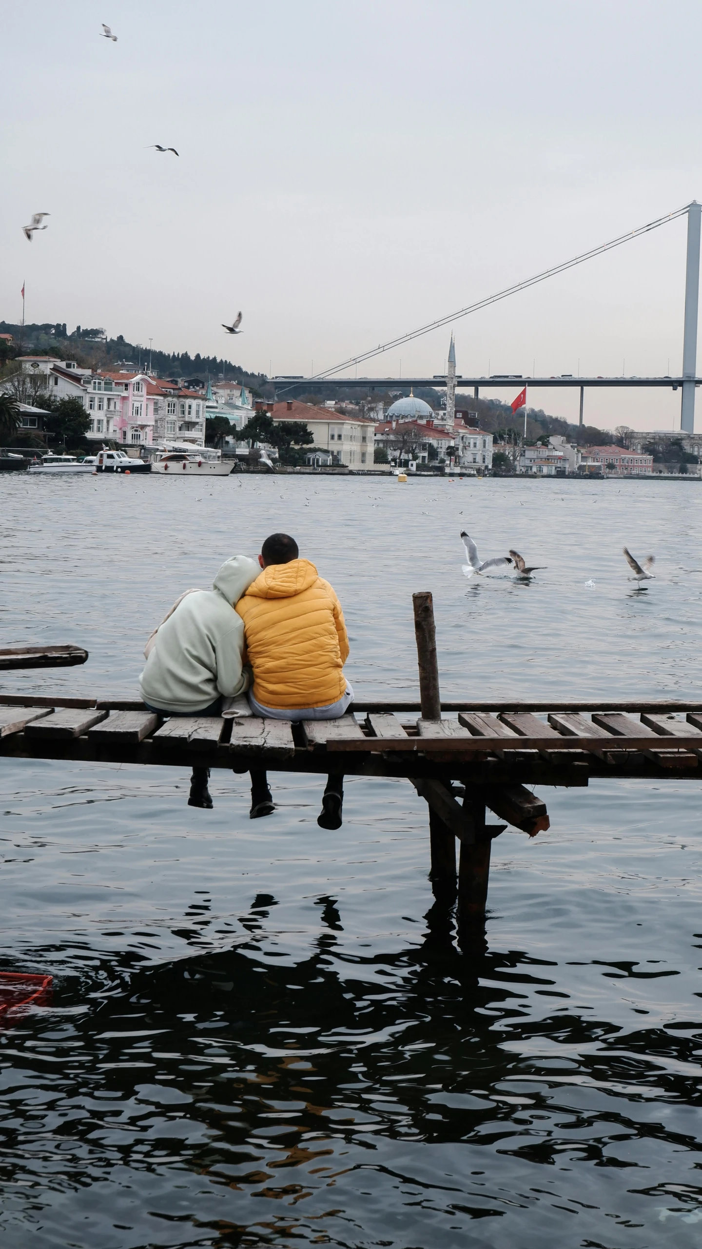 a couple of people that are sitting on a dock, by irakli nadar, pexels contest winner, hurufiyya, istanbul, a cold, color footage, bridge