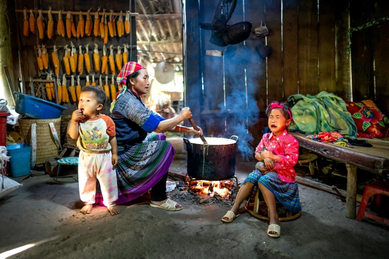 a woman and two children cooking over an open fire, by Dan Content, pexels contest winner, in style of lam manh, avatar image, inside house in village, multicoloured