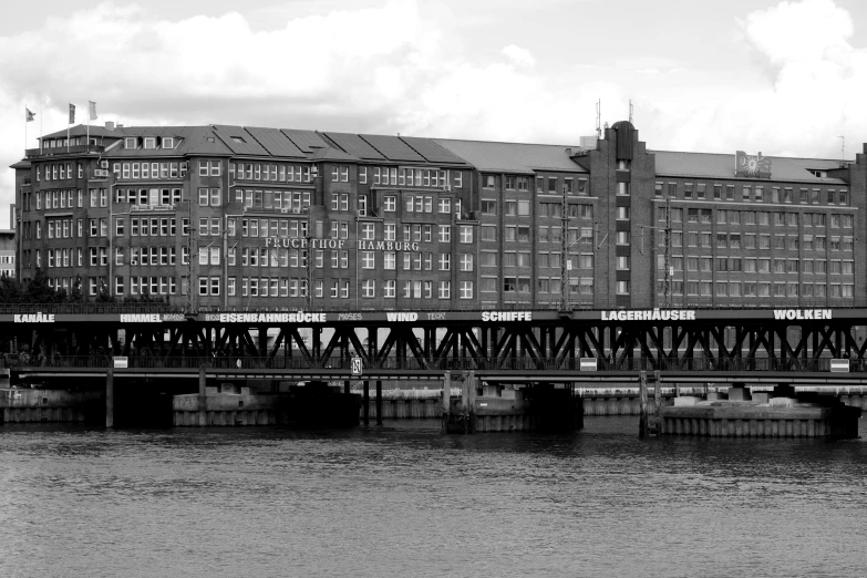 a black and white photo of a train crossing a bridge, by Kristian Zahrtmann, pexels contest winner, art nouveau, warehouses, viewed from the harbor, berlin, july 2 0 1 1