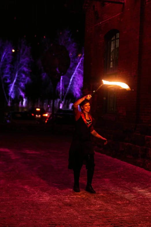 a man holding a fire stick in front of a building, by Gwen Barnard, unsplash, kinetic art, a sorceress casting a ice ball, purple scene lighting, roaming entertainers, 15081959 21121991 01012000 4k