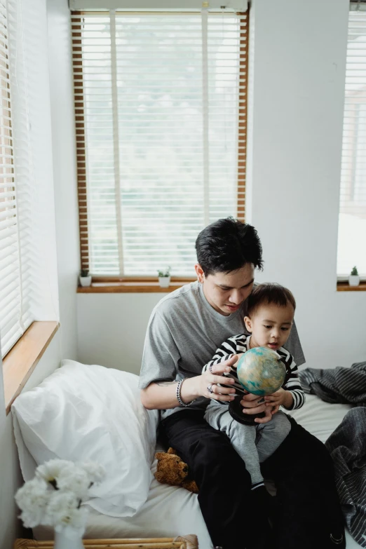 a man sitting on a bed holding a small child, pexels contest winner, visual art, globes, jakarta, window light, 1 2 9 7