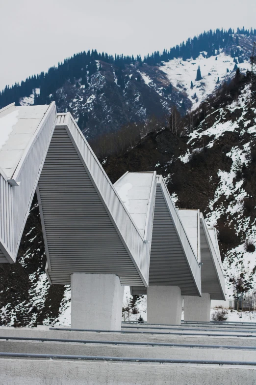 a man riding a snowboard down the side of a snow covered slope, inspired by Peter Zumthor, modernism, metallic bridge, simple gable roofs, white concrete, neo - andean architecture