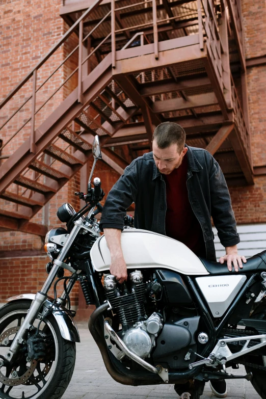 a man standing next to a parked motorcycle, white mechanical details, thinning hair, lachlan bailey, profile image