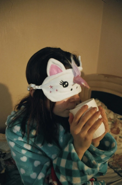 a woman sitting on a bed drinking from a cup, inspired by Elsa Bleda, pexels contest winner, kitsune mask on head, pony, low quality photo, kid