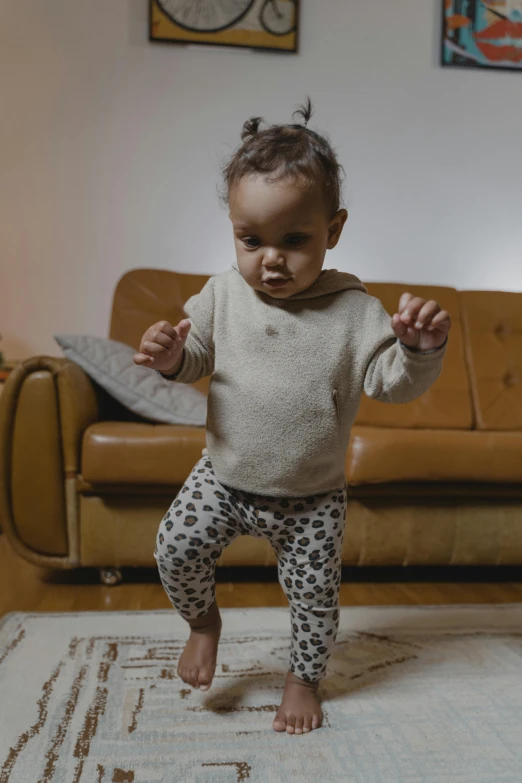 a baby standing on a rug in a living room, by Nina Hamnett, pexels contest winner, arabesque, she is dancing, wearing a hoodie and sweatpants, knees upturned, spotted