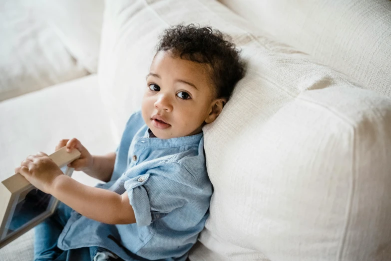 a baby sitting on a couch holding a book, pexels contest winner, happening, light-brown skin, looking at his phone, kid named finger, resting on a pillow