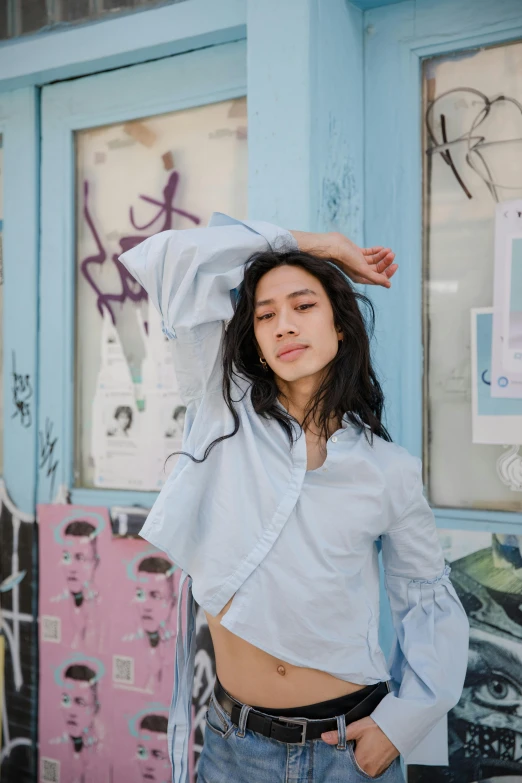 a woman standing in front of a blue building, an album cover, inspired by Ren Hang, trending on pexels, button - up shirt, gemma chan girl portrait, pastelwave, white sleeves