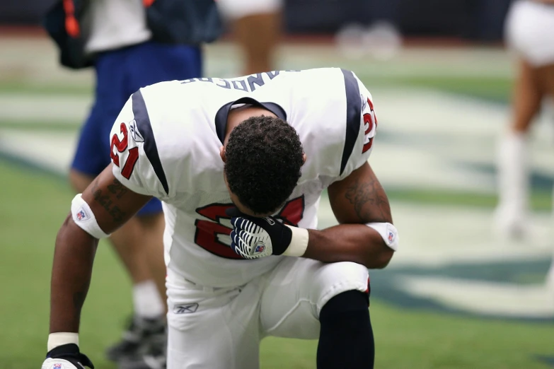 a football player kneels down on the field, a tattoo, by Paul Davis, pexels, head bowed slightly, patriotism, j. h. williams iii, 🇺🇦