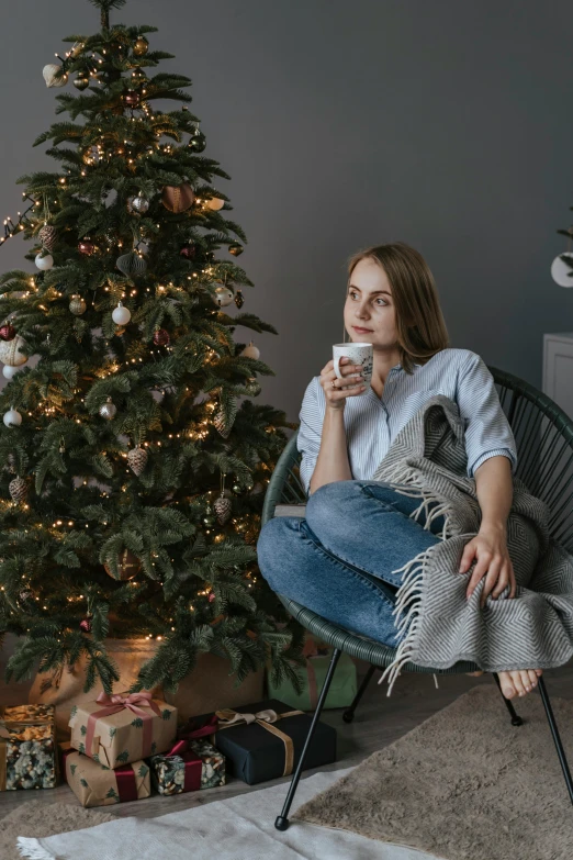 a woman sitting in a chair in front of a christmas tree, woman drinking coffee, wearing a dark shirt and jeans, anna podedworna, promo image