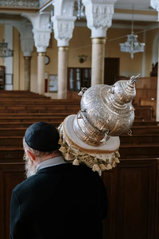 a man with a hat on his head in a church, an album cover, by Konrad Witz, trending on unsplash, mosque synagogue interior, overturned ornate chalice, hebrew, holding helmet