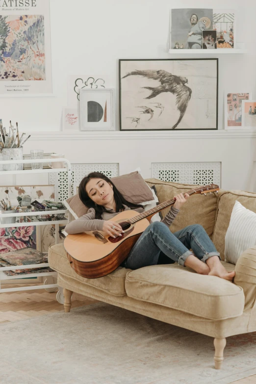 a woman sitting on a couch playing a guitar, inspired by Mandy Jurgens, madison beer, curated collections, in her room, profile image