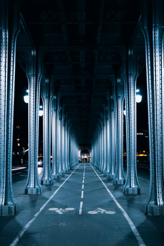 an empty street under a bridge at night, an album cover, inspired by Thomas Struth, unsplash contest winner, tall columns, musee d'orsay 8 k, detailed symmetrical, metallic light