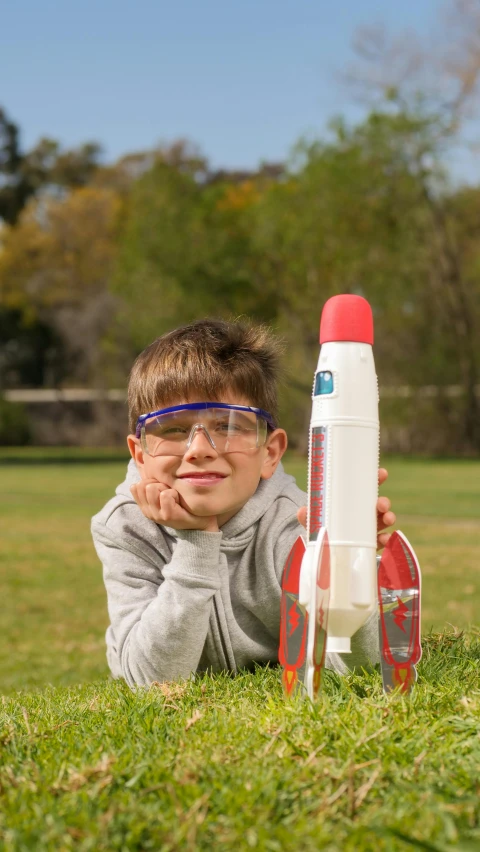 a young boy laying in the grass with a toy rocket, pexels, photorealism, wearing lab coat and glasses, avatar image, rocket launching, beaker