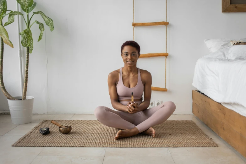 a woman sitting on the floor in a yoga pose, a portrait, pexels contest winner, with brown skin, holding a wooden staff, wearing a tracksuit, relaxing environment