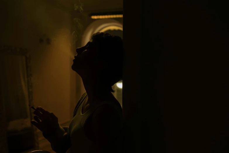 a person smoking a cigarette in a dark room, inspired by Nan Goldin, pexels contest winner, light and space, detailed silhouette, as she looks up at the ceiling, praying with tobacco, ( ( theatrical ) )