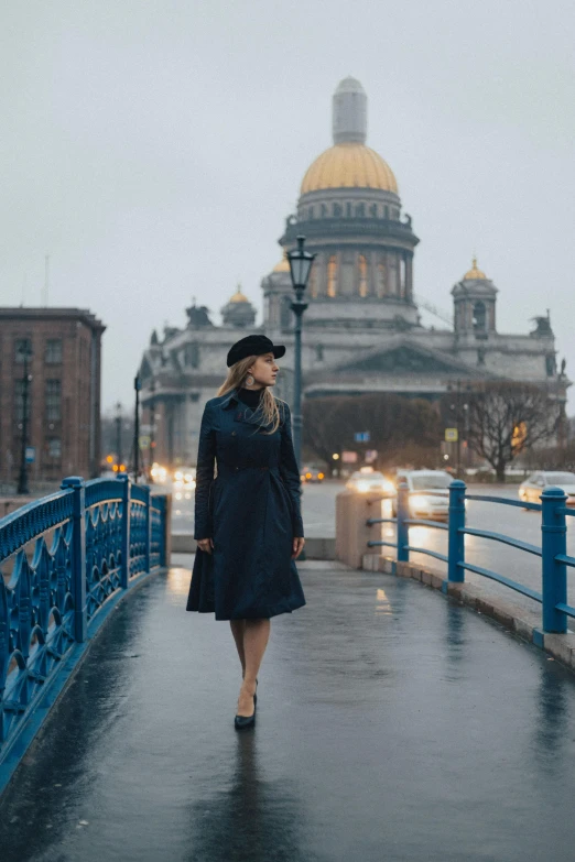 a woman walking across a bridge in the rain, a portrait, by Julia Pishtar, pexels contest winner, socialist realism, with great domes and arches, navy, russian clothes, trench coat