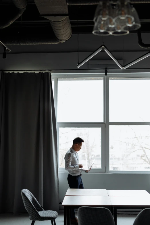 a man standing at a table in front of a window, modern aesthetic, curtains, office ceiling panels, 2019 trending photo