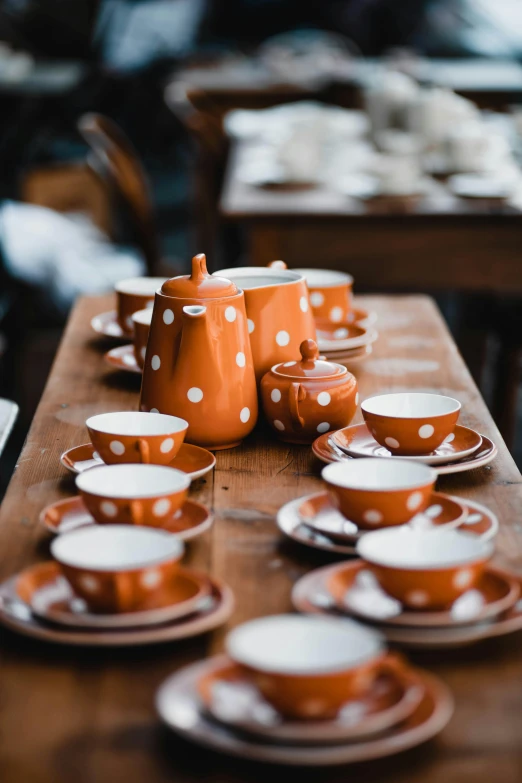 a wooden table topped with cups and saucers, by Lee Loughridge, unsplash, mingei, polka dot, orange hue, made of glazed, highest quality