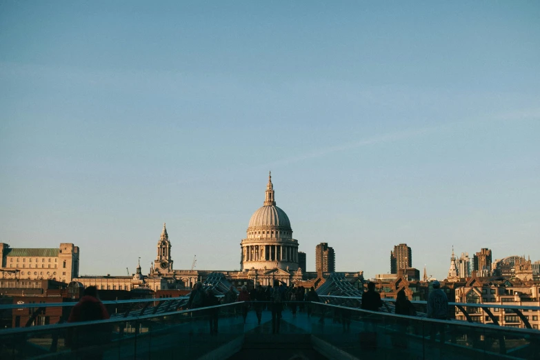 a group of people walking across a bridge, by Christopher Wren, pexels contest winner, black domes and spires, skyline showing, clear blue skies, evening sunlight