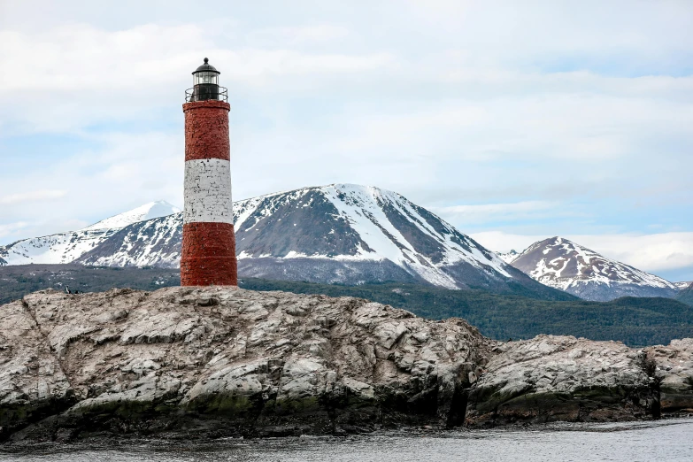 a red and white lighthouse sitting on top of a rock, snow capped mountains, covered in coral and barnacles, andes, listing image