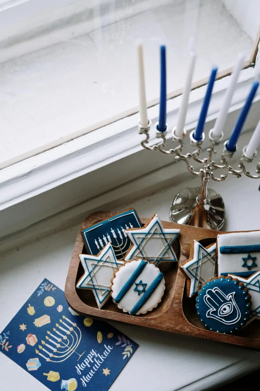 a tray of cookies and a menorah on a window sill, a still life, by Julia Pishtar, pexels, dau-al-set, white and blue, handcrafted, fully decorated, instagram story