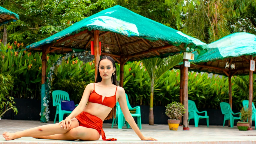 a woman in a red bikini sitting on the edge of a pool, a portrait, pexels contest winner, philippines, avatar image, wearing crop top and miniskirt, lush surroundings