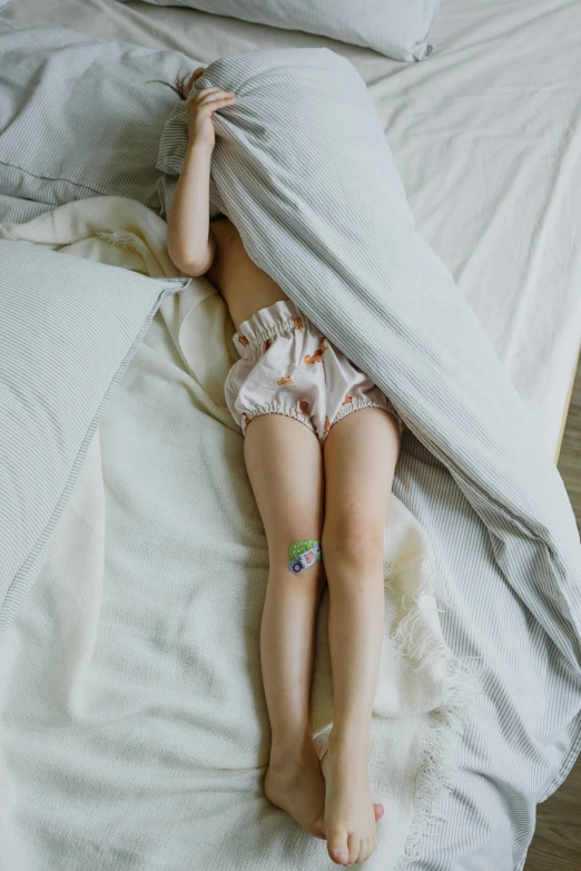 a little girl laying on top of a bed under a blanket, unsplash, renaissance, short puffy pants made of silk, intertwined full body view, ignant, tired