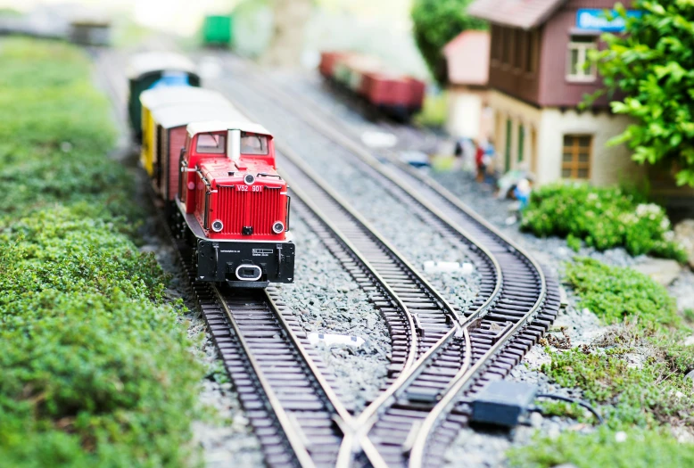 a red train traveling down train tracks next to a small house, a tilt shift photo, unsplash, figuration libre, toys, 🚿🗝📝