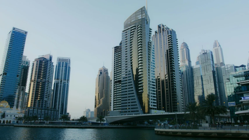 a group of tall buildings next to a body of water, inspired by Zaha Hadid, hurufiyya, middle east, low quality photo, early evening, low iso