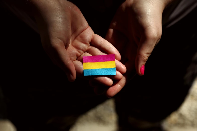 a person holding a piece of paper in their hands, by Julia Pishtar, unsplash, hurufiyya, lgbt flag, 15081959 21121991 01012000 4k, resin, a wooden