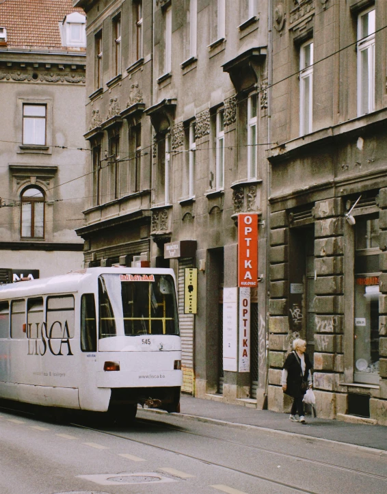 a white bus driving down a street next to tall buildings, a photo, viennese actionism, bogna gawrońska, gif, photo for a store, trams ) ) )