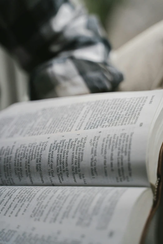 a person sitting on a bench reading a book, biblical clothing, up close, grey, unreadable