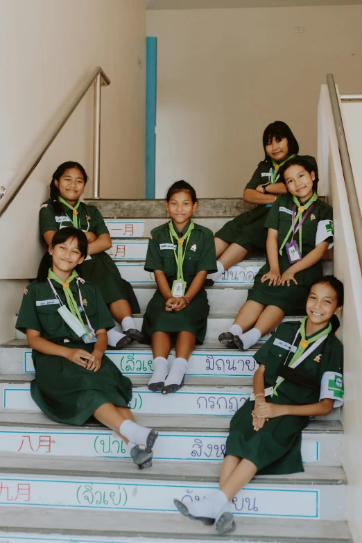 a group of girls sitting on top of a flight of stairs, patiphan sottiwilai, wearing green, high school badge, 5 years old