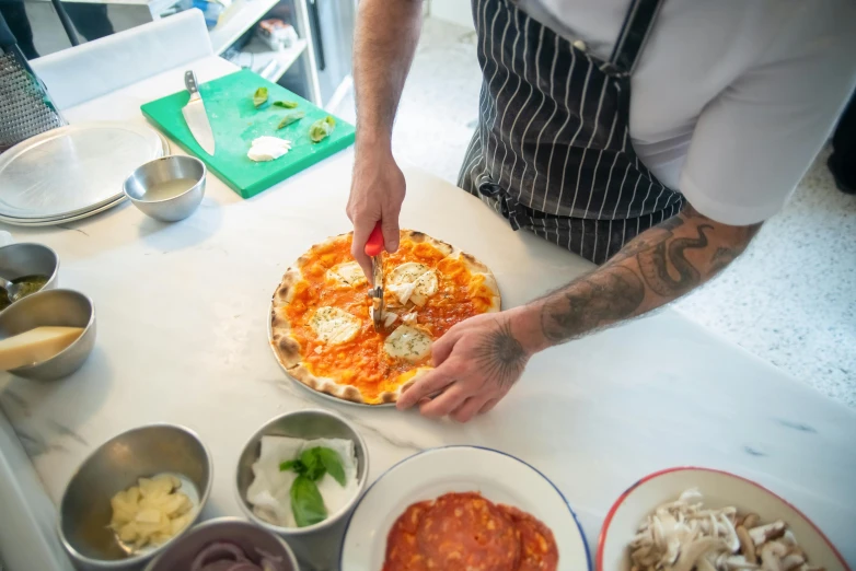 a chef is putting toppings on a pizza, by Tom Bonson, lachlan bailey, lots of mozzarella balls, all marble, in house