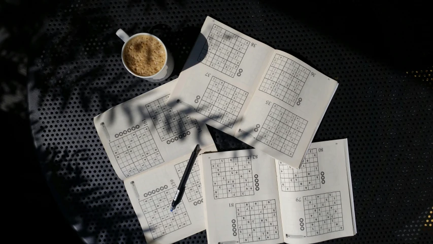 a pile of papers sitting on top of a table next to a cup of coffee, a jigsaw puzzle, mingei, grid layout, thumbnail, outdoor photo, black squares on 4 corners