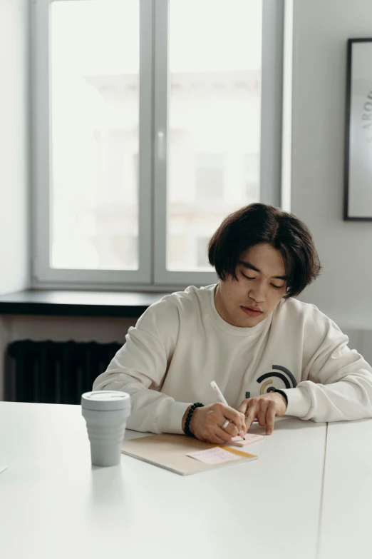 a man sitting at a table writing on a piece of paper, inspired by jeonseok lee, pexels contest winner, arbeitsrat für kunst, non binary model, off - white collection, gif, confident looking