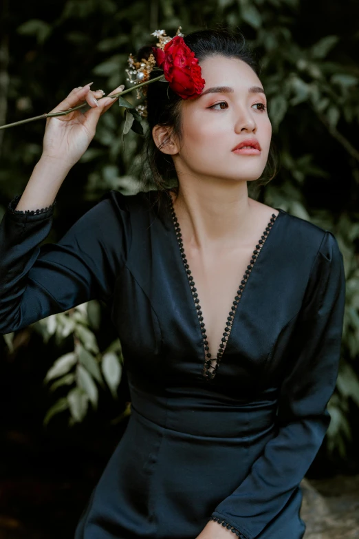 a woman in a black dress with a flower in her hair, an album cover, inspired by Ruth Jên, unsplash, indonesia, puff sleeves, silk robes, wearing a cocktail dress