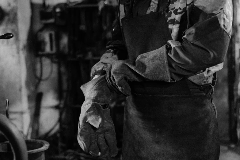 a black and white photo of a man in an apron, by Kristian Zahrtmann, pexels, arbeitsrat für kunst, wearing metal gauntlet, in a workshop, detail, made of bronze