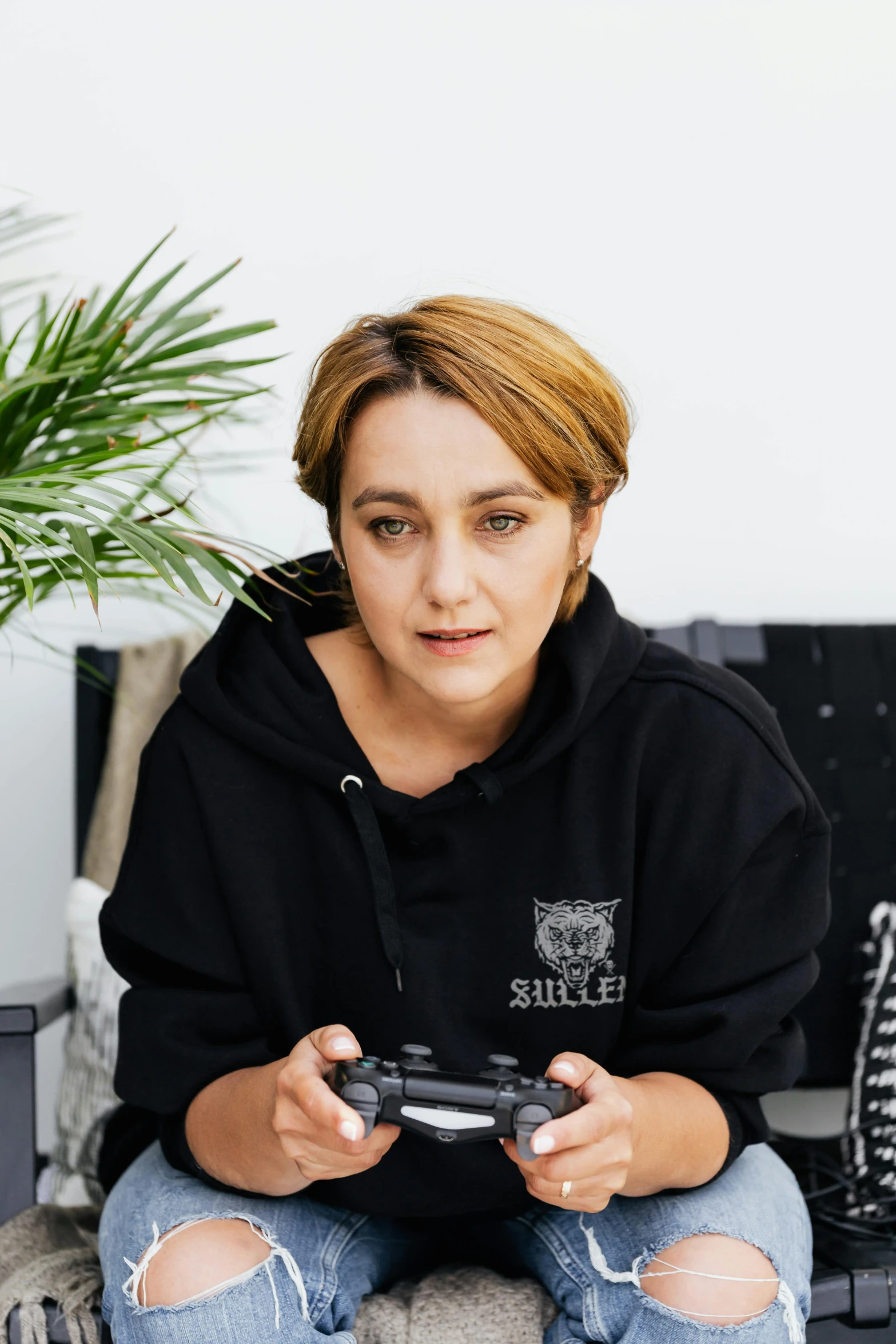 a woman sitting on a couch holding a video game controller, inspired by Zoë Mozert, looking serious, lachlan bailey, profile image, portrait photo