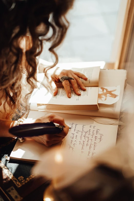 a woman sitting at a table writing on a piece of paper, by Julia Pishtar, pexels contest winner, books covered in jewels, singer songwriter, thumbnail, an open book