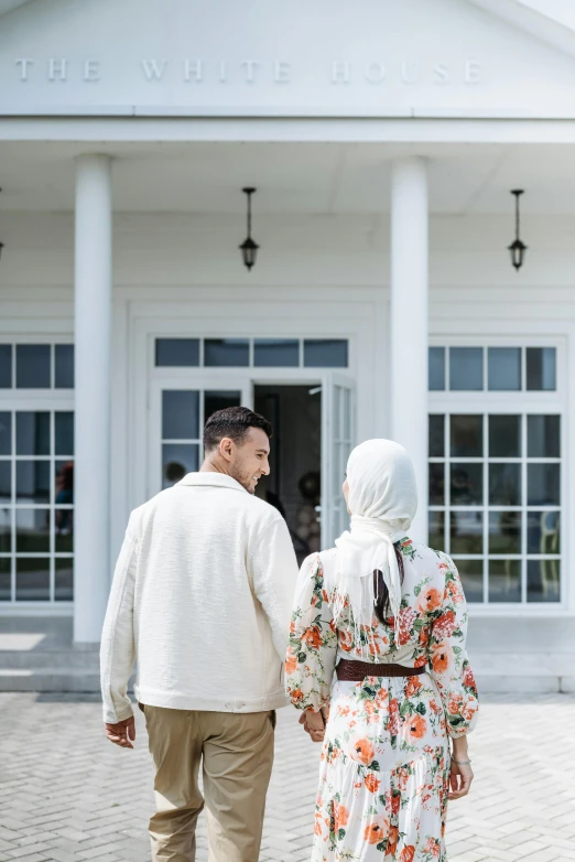 a man and a woman walking in front of a building, a colorized photo, unsplash, hurufiyya, wearing white clothes, background image, pastoral, in house