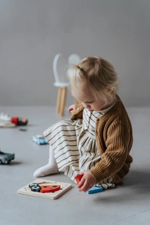 a little girl sitting on the floor playing with toys, pexels contest winner, scandinavian design, cardigan, striped, sustainable materials