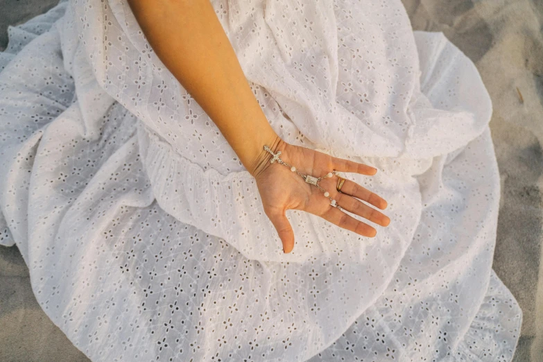 a woman sitting on top of a sandy beach, unsplash, visual art, silver bracelets, wearing a hospital gown, perfect hands, dress in voile