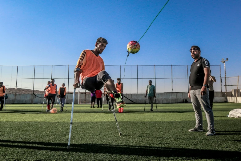 a man kicking a soccer ball on top of a field, a picture, by Youssef Howayek, trending on dribble, dau-al-set, crutches, one legged amputee, holding a cane, ap news photo