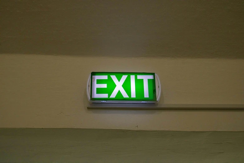 a green exit sign mounted to the side of a wall, pexels, fluorescent ceiling lights, paul barson, jets, next gen
