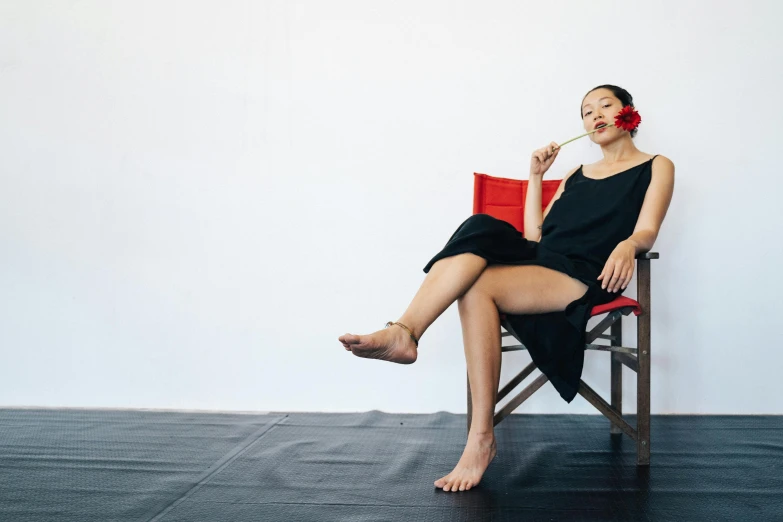 a woman sitting in a chair reading a book, a portrait, inspired by Fei Danxu, unsplash, minimalism, playful pose of a dancer, black and red silk clothing, 5 feet away, vietnamese woman