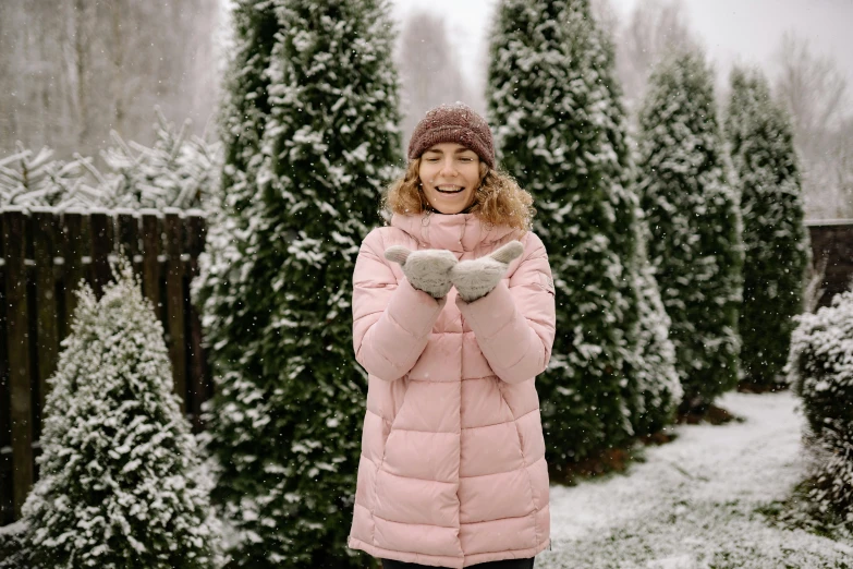 a woman in a pink coat holding a teddy bear, by Emma Andijewska, pexels, snow on trees and ground, excited russians, against a winter garden, puffer jacket