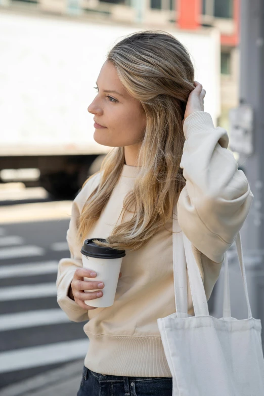 a woman walking down the street holding a cup of coffee, shoulder - length blonde hair, wearing sweatshirt, thoughtful ), exiting store