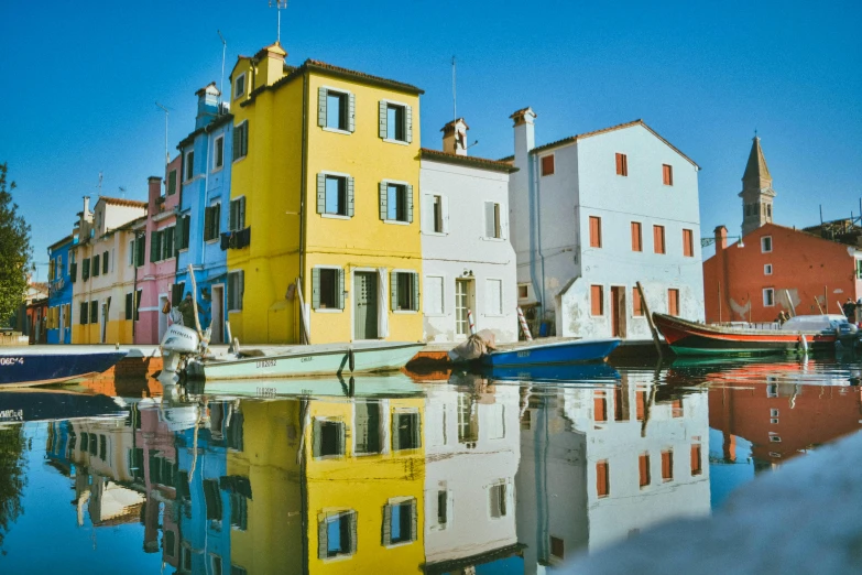 a row of colorful buildings next to a body of water, a photo, inspired by Wes Anderson, pexels contest winner, hyperrealism, vouge italy, fishing village, water reflections, bright sunny day